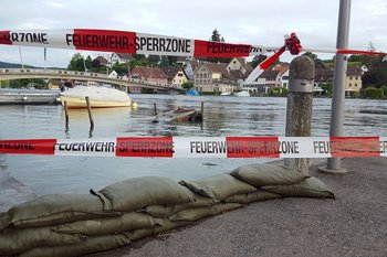 Eine Feuerwehrabsperrung an einer vom Hochwasser gefluteten Straße in Flussnähe. Beispielbild